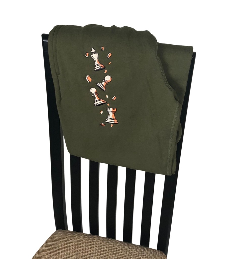 Olive Pawn Chip Sweatpants by Smothered Mate folded over a chair